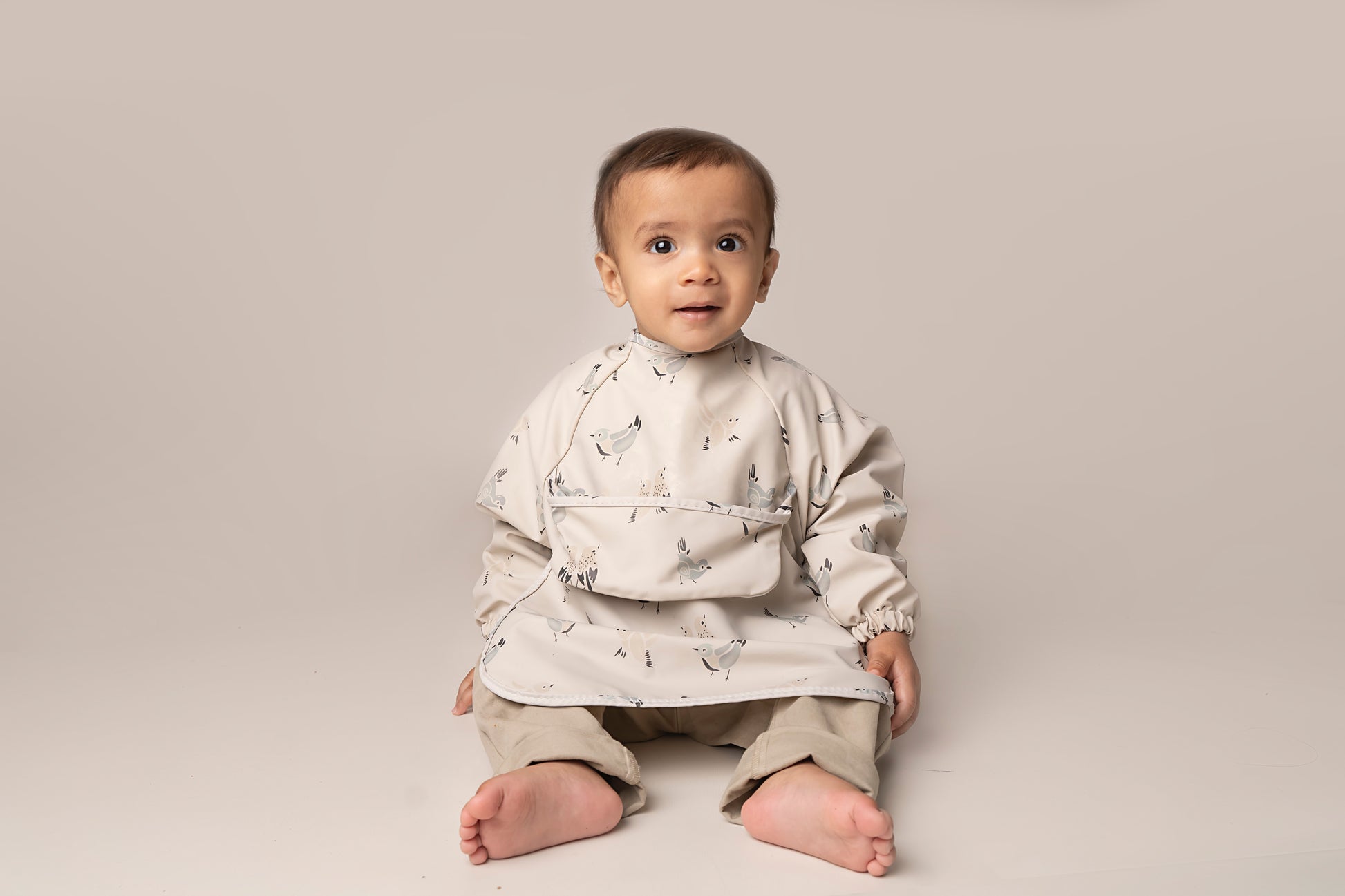 A practical long sleeve weaning bib with elasticated cuffs, designed to handle messes from food, paint, and playtime fun. The bib features a catch-all pocket to prevent spills and splatters, along with a double-button neck fastening for a secure fit and easy dressing. It's waterproof and machine washable for quick cleanup.