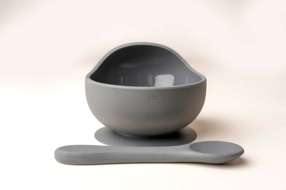 A baby weaning Suction Bowl + Spoon Set designed to make weaning easier and help babies and toddlers establish mealtime independence. The set features a raised side to assist child in scooping up food independently. It has a strong suction base to prevent spills and overturned bowls. Made from BPA and Phthalate-free, non-toxic food-grade silicone, it is unbreakable, waterproof, and easy to clean. Microwave and dishwasher safe.
