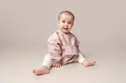  A practical long sleeve weaning bib with elasticated cuffs, designed to handle messes from food, paint, and playtime fun. The bib features a catch-all pocket to prevent spills and splatters, along with a double-button neck fastening for a secure fit and easy dressing. It's waterproof and machine washable for quick cleanup.