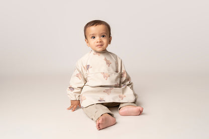  A practical long sleeve weaning bib with elasticated cuffs, designed to handle messes from food, paint, and playtime fun. The bib features a catch-all pocket to prevent spills and splatters, along with a double-button neck fastening for a secure fit and easy dressing. It's waterproof and machine washable for quick cleanup.