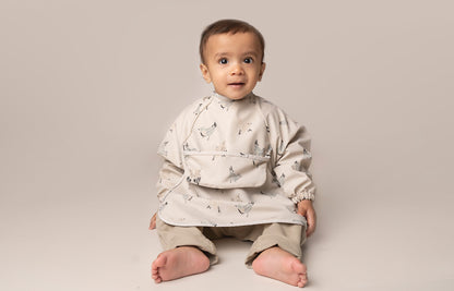  A practical long sleeve weaning bib with elasticated cuffs, designed to handle messes from food, paint, and playtime fun. The bib features a catch-all pocket to prevent spills and splatters, along with a double-button neck fastening for a secure fit and easy dressing. It's waterproof and machine washable for quick cleanup.